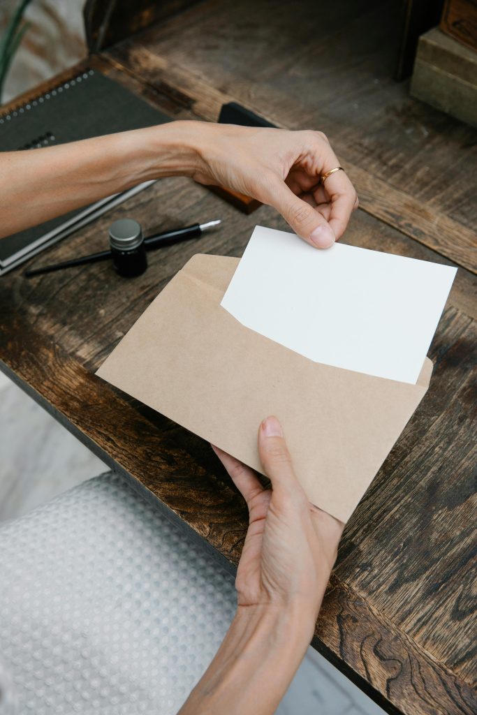 Close-up of woman handling a blank card and envelope at a rustic desk.