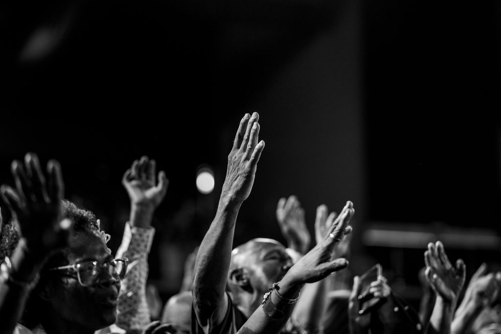 Monochrome photo capturing a group with hands raised in prayer and worship.