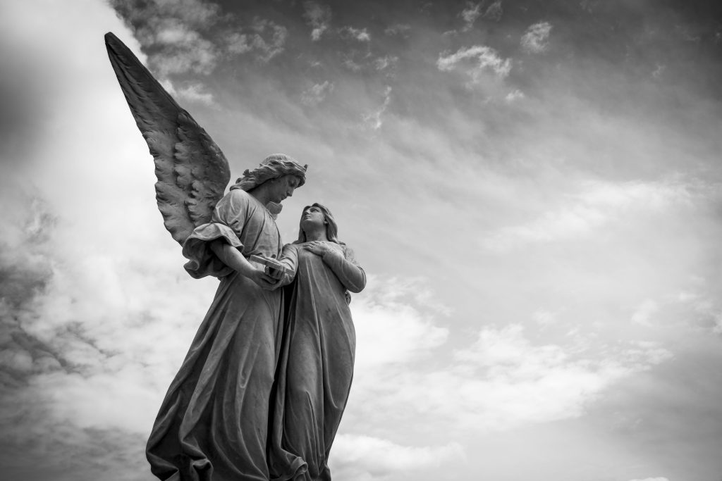 Striking black and white photo of angelic sculptures under dramatic clouds.
