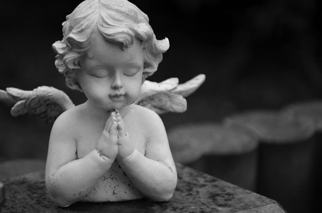 A grayscale close-up of a serene angel sculpture with folded hands in prayer.